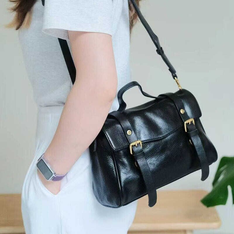 Woman wearing a black leather satchel crossbody bag with gold buckle over shoulder