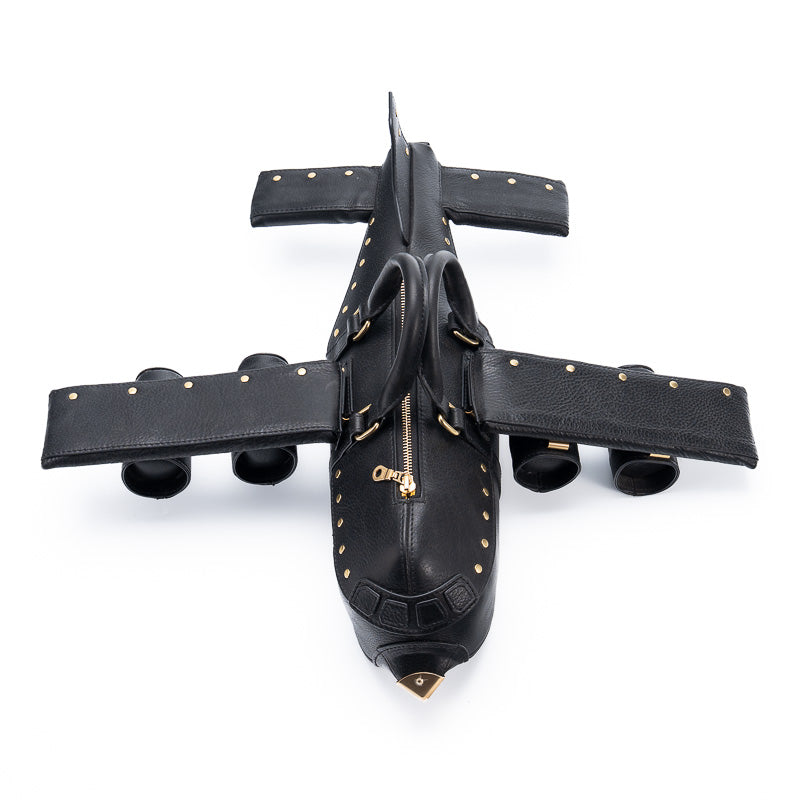 Black airplane-shaped leather handbag with gold studs and brass nose cone, top view