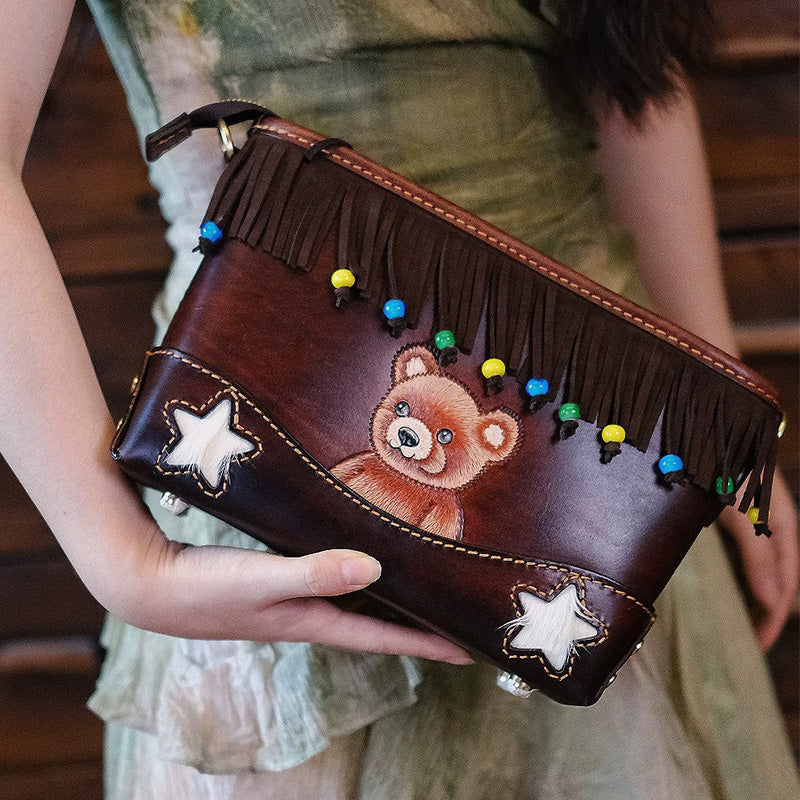 Woman holding a leather crossbody bag with bear artwork and colorful beaded fringe.