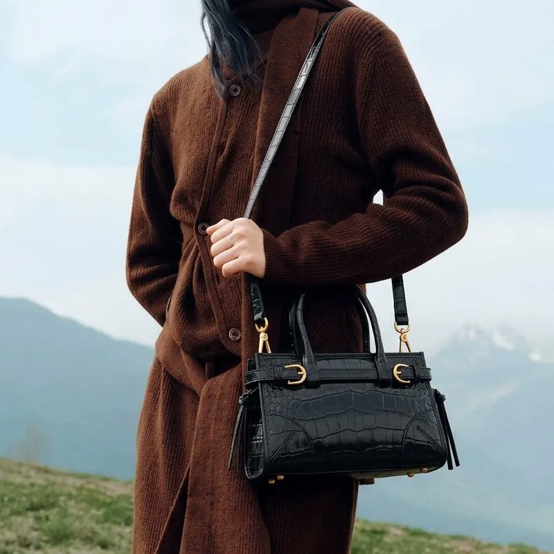 Woman wearing a black croc-embossed leather satchel over her shoulder outdoors.