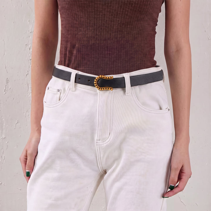 Woman wearing a black leather belt with a gold-tone beaded buckle and white jeans.