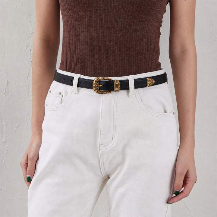 Woman wearing a black leather belt with an ornate gold-tone buckle and white jeans.