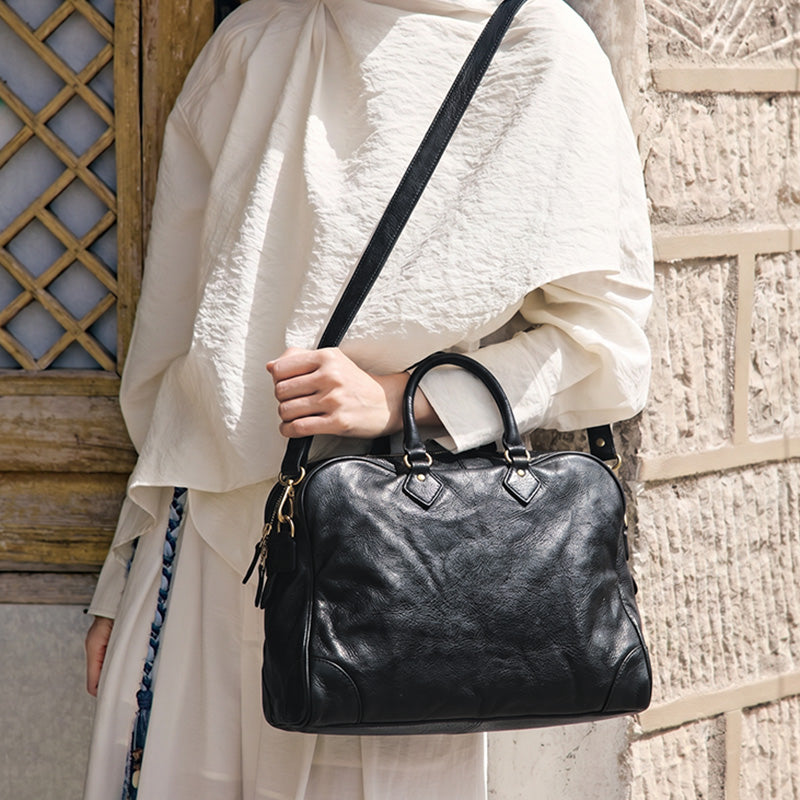 Model wearing a black leather Boston bag with dual top handles and a shoulder strap.