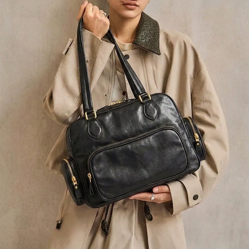 Model holding a black leather Boston bag with front and side zip pockets.