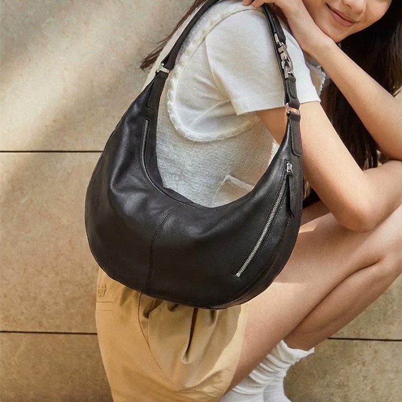 Model wearing a black leather crescent hobo bag with a side zip pocket over her shoulder.