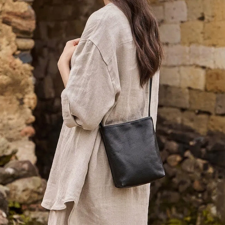 Woman wearing a small black leather crossbody bag with a beige outfit.