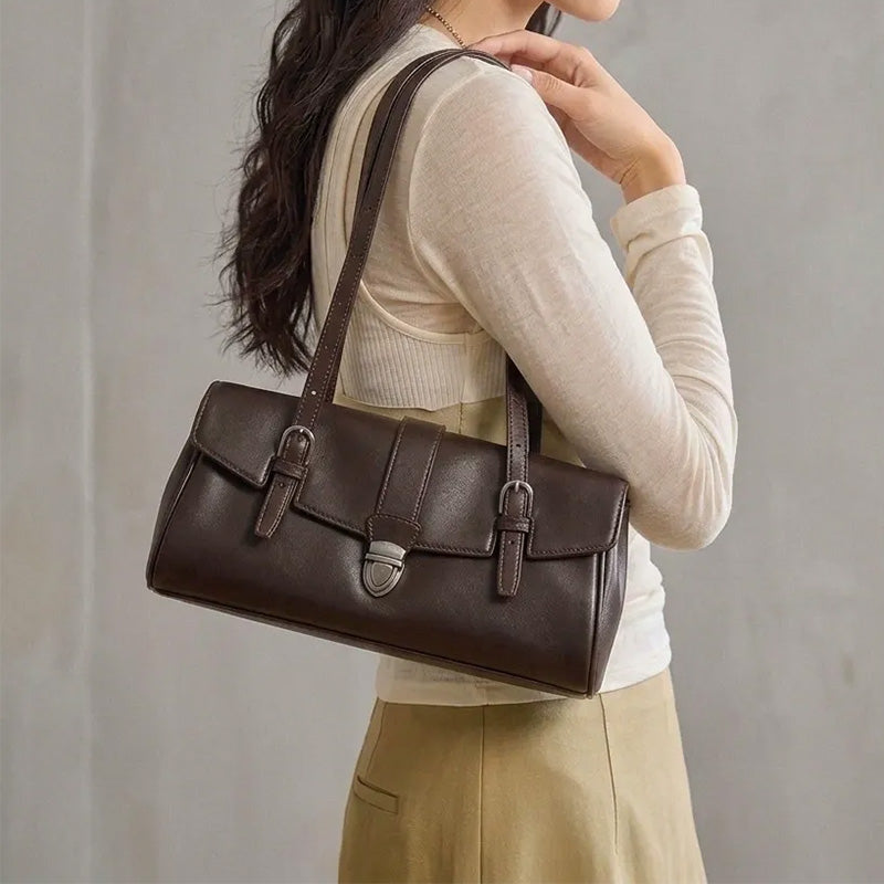 Woman wearing a dark brown leather east-west shoulder bag with a flap and metal clasp.