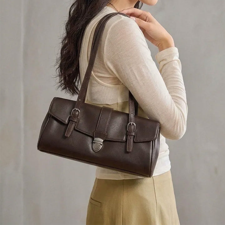 Woman wearing a dark brown leather east-west shoulder bag with a flap and metal clasp.