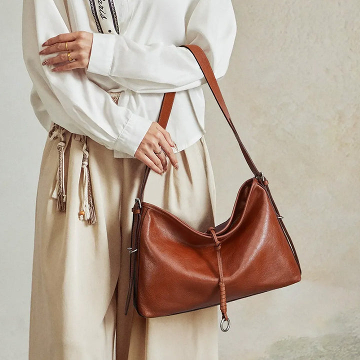 Model carrying a brown leather hobo bag with a slouchy shape and metal ring detail.