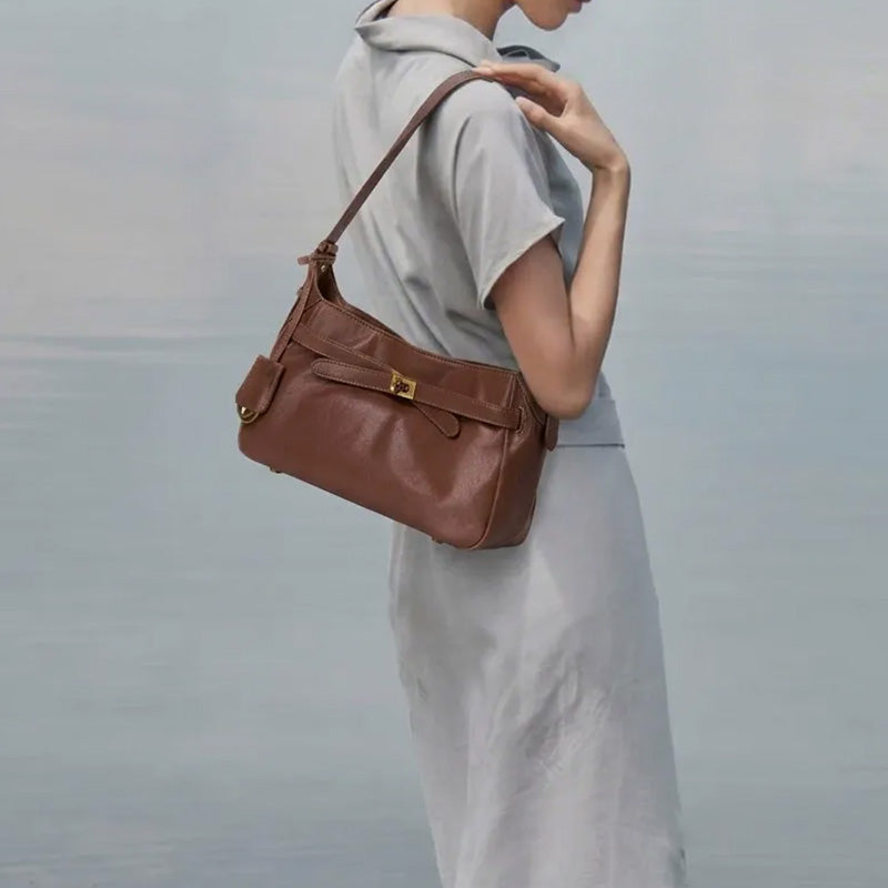 Model carrying a brown leather hobo shoulder bag with a brass turn-lock.