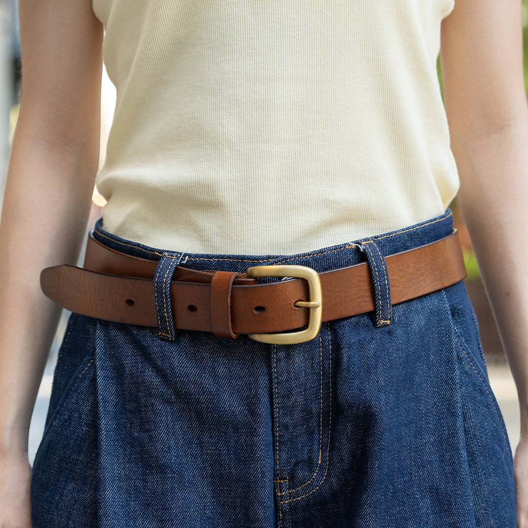 Woman wearing a brown leather belt with a gold-tone pin buckle and blue jeans.