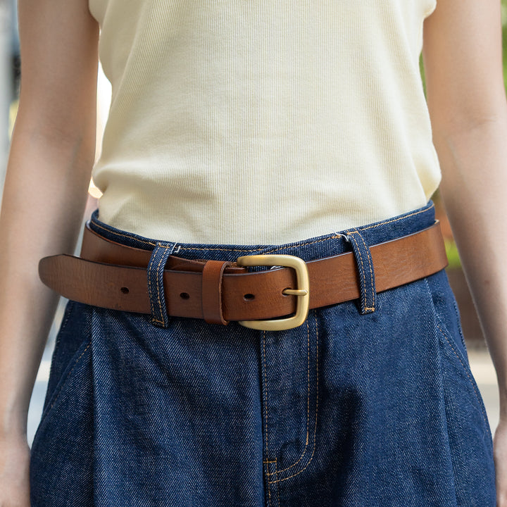 Woman wearing a brown leather belt with a gold-tone pin buckle and blue jeans.