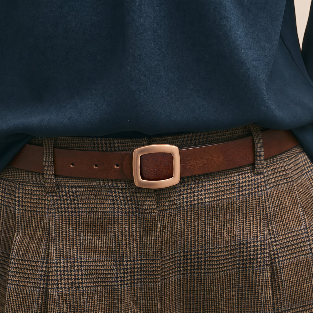 Brown leather belt with a gold-tone square buckle worn with plaid trousers.
