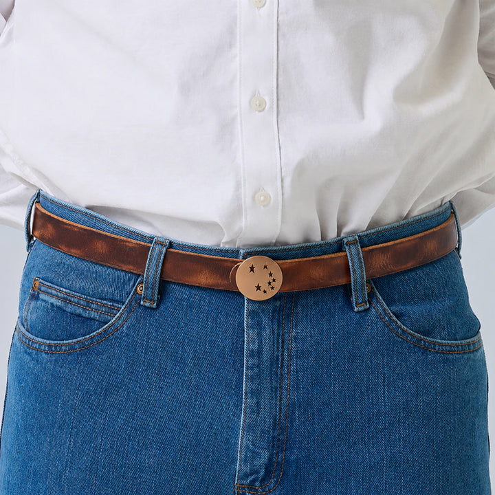 Brown leather belt with a round star-cutout buckle worn with blue jeans and a white shirt.
