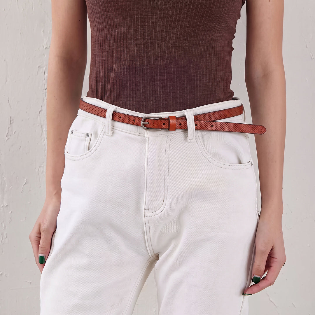 Woman wearing a brown skinny leather belt with a silver-tone pin buckle and white jeans.