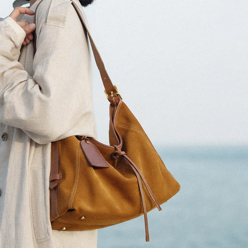 Model wearing a brown suede hobo shoulder bag with leather trim and tie accents.