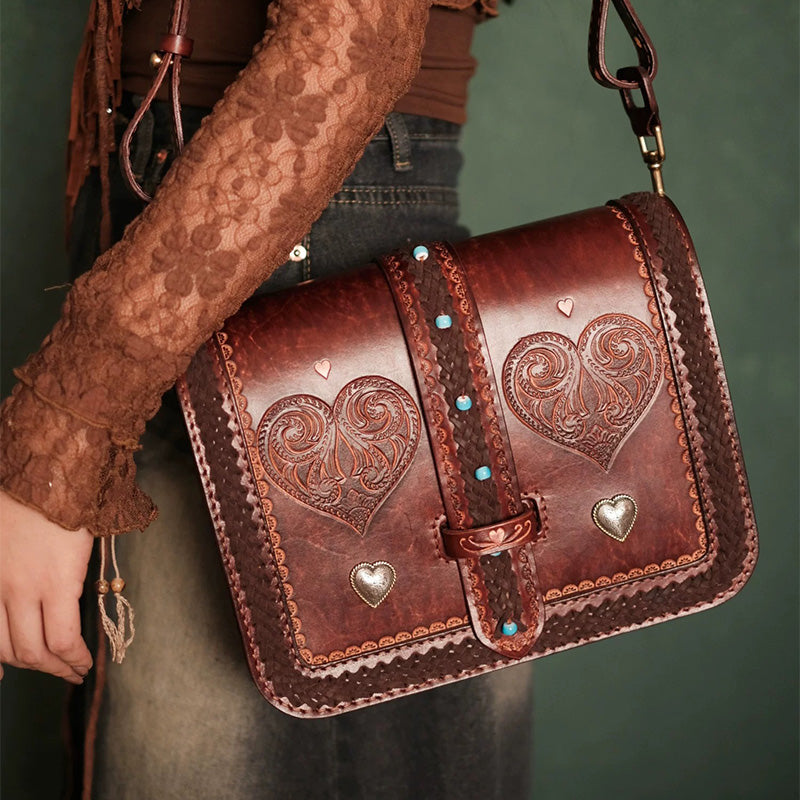 Model wearing a brown tooled leather crossbody bag with heart motifs and braided trim.