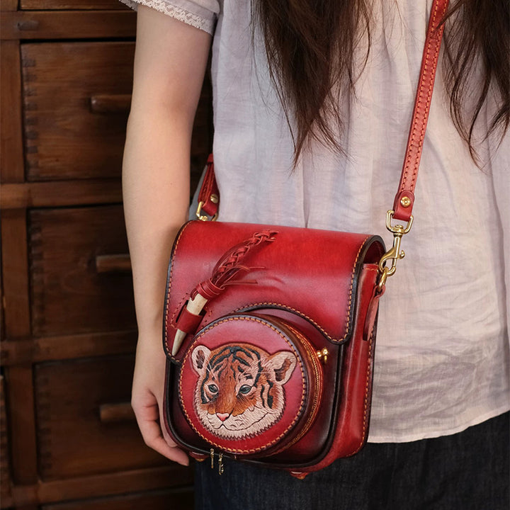 Model wearing a burgundy leather flap crossbody bag with a round tiger pouch.
