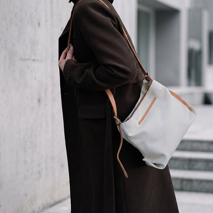 Model carrying white canvas crossbody bag from behind.