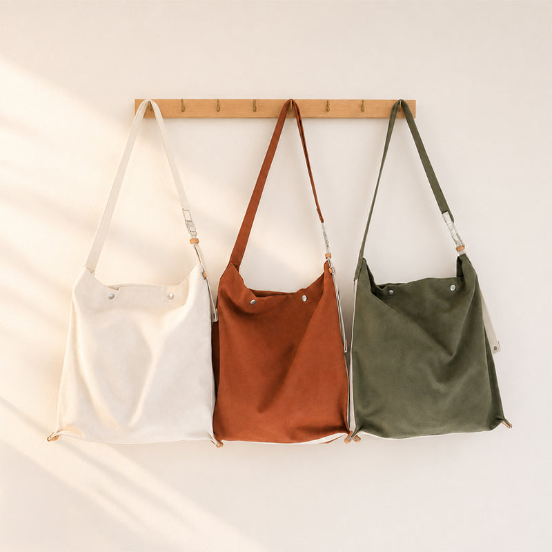 Canvas hobo crossbody bag in white, honey brown, and dark green hanging on a wooden rack