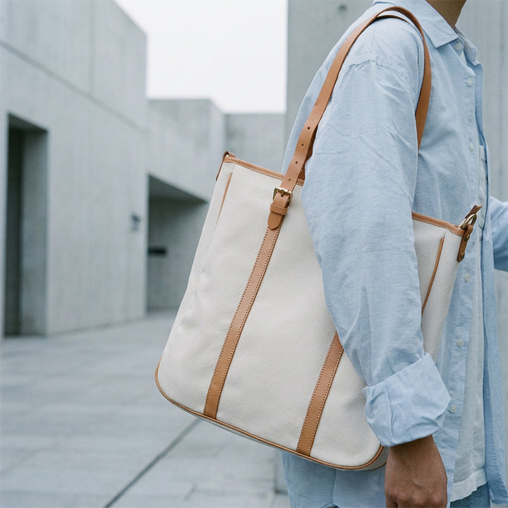 White canvas tote bag with leather harness straps worn over shoulder outdoors