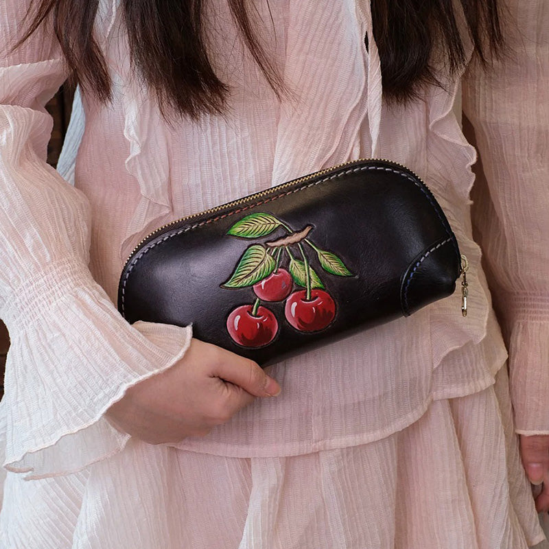 Woman holding a black cherry leather clutch bag with hand-tooled fruit detail.