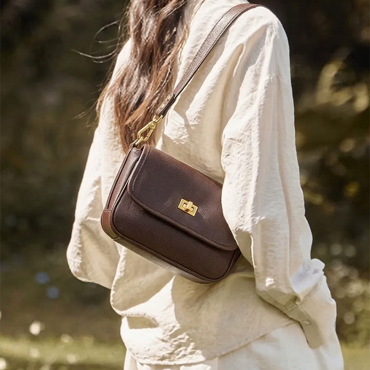 Woman wearing a coffee brown leather flap crossbody bag with a gold-tone twist lock.