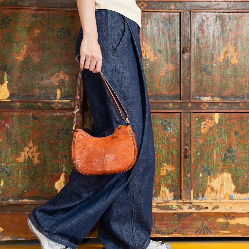 Woman carrying a brown full grain leather crescent bag on shoulder, side view