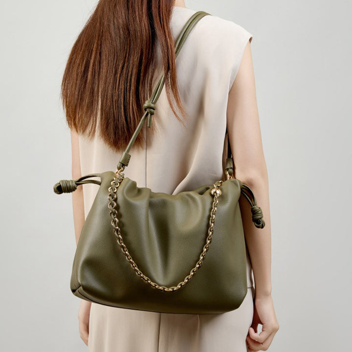 A woman wears a dark green leather bucket bag with a gold-tone chain accent over her shoulder.
