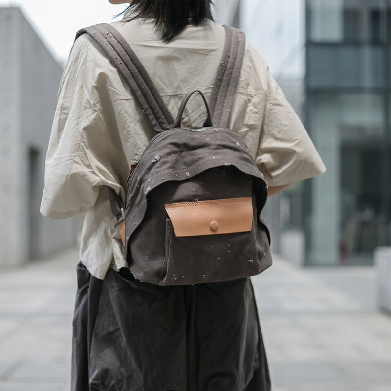 Woman wearing a distressed canvas mini backpack with leather snap pocket on city street