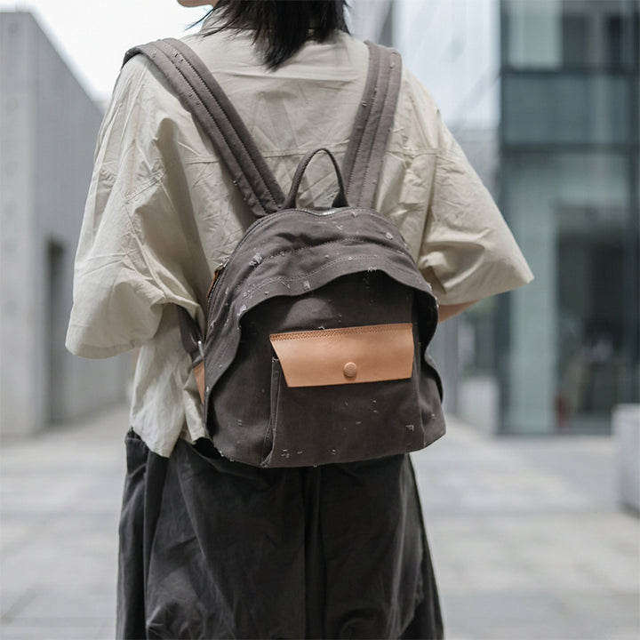Woman wearing a distressed canvas mini backpack with leather snap pocket on city street
