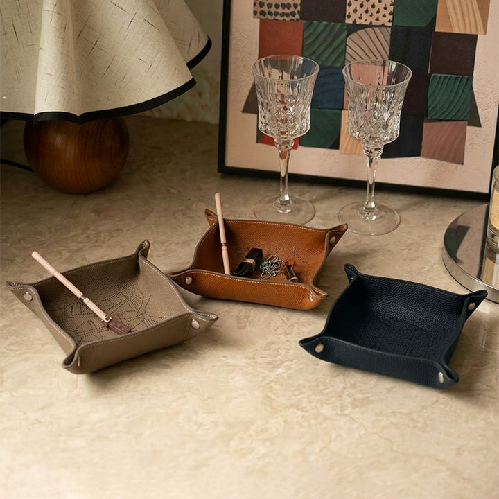 Three embossed leather catchall trays in gray, brown and black styled on a home surface