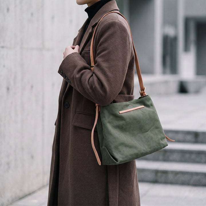 Model styling green canvas crossbody bag with dark coat.