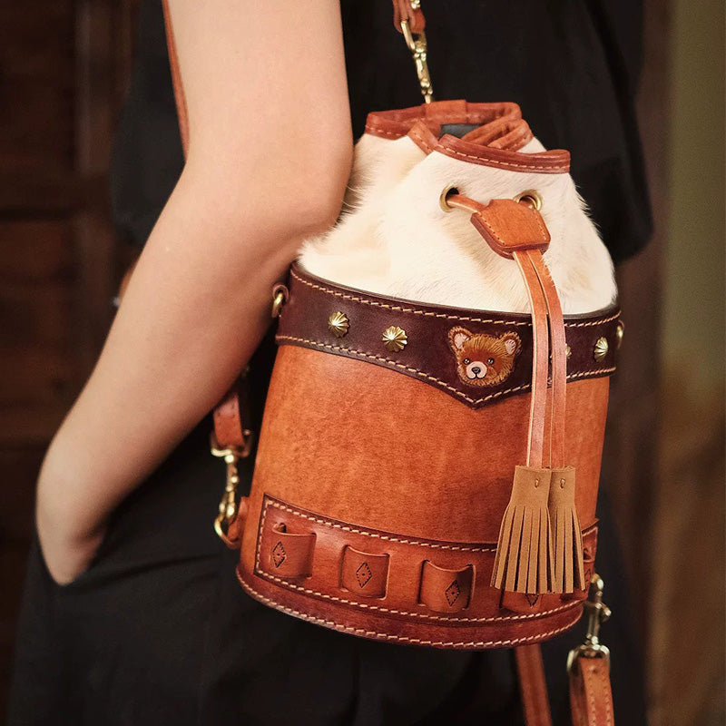 Woman carrying a brown leather bucket bag with a hair-on-hide top and drawstring tassels.