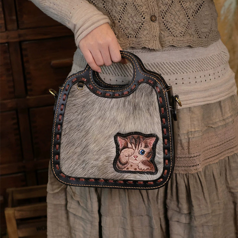 Person holding a hair-on-hide top handle bag with a carved kitten on the front.