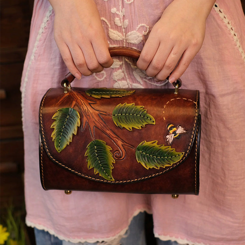 A woman carries a hand-carved leather barrel bag with leaf and bee artwork.