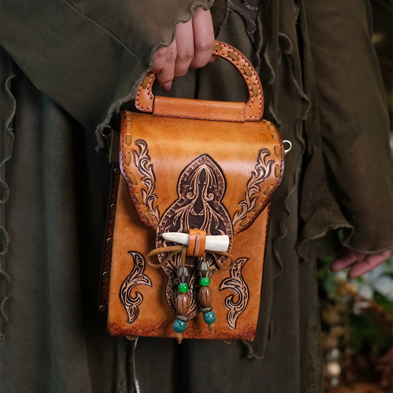 A hand-tooled brown leather box crossbody bag with a top handle.