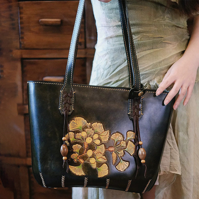 Woman carrying a hand-tooled leather ginkgo tote bag in vintage black.