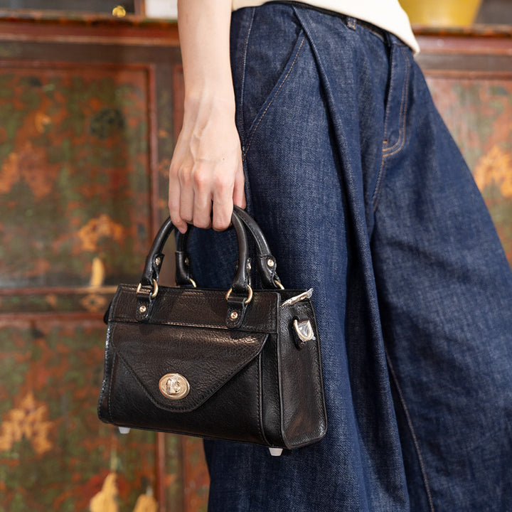 Woman holding a black horsehide leather satchel bag with gold twist lock flap pocket, side view