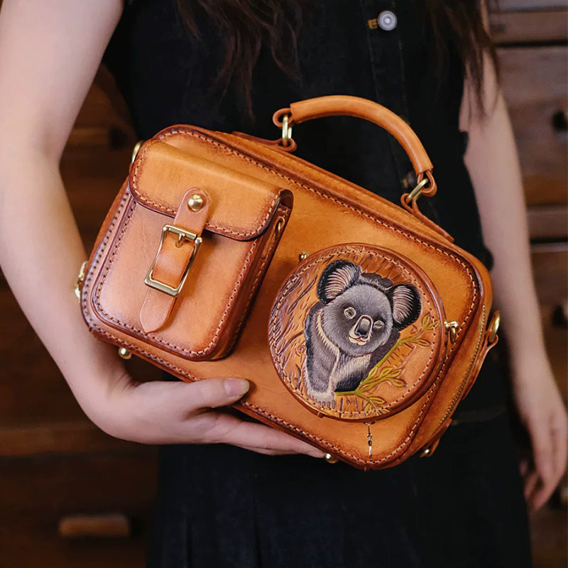 Woman holding a brown leather camera bag with a koala pouch on the front.