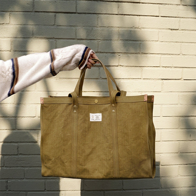 Oversized khaki green canvas tote bag held by hand, heavy duty with brass rivets
