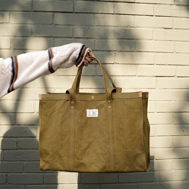 Oversized khaki green canvas tote bag held by hand, heavy duty with brass rivets