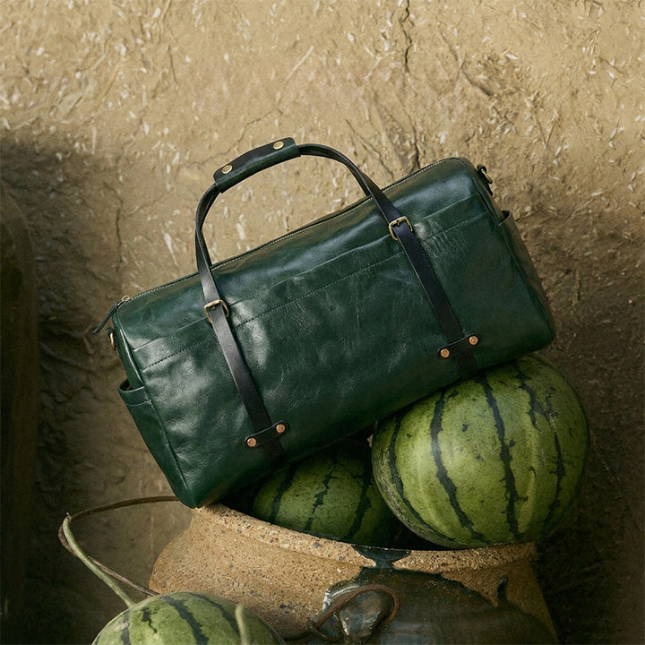 Large green leather duffle bag with gold hardware and dual handles, crafted from vegetable-tanned leather for travel.