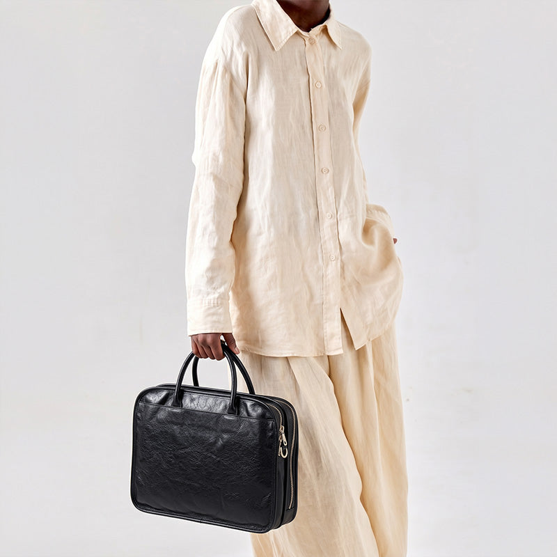 Black vegetable-tanned leather briefcase with multi-compartment zipped layout, gold rivet handle, and laptop sleeve for work.
