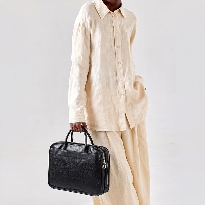 Black vegetable-tanned leather briefcase with multi-compartment zipped layout, gold rivet handle, and laptop sleeve for work.