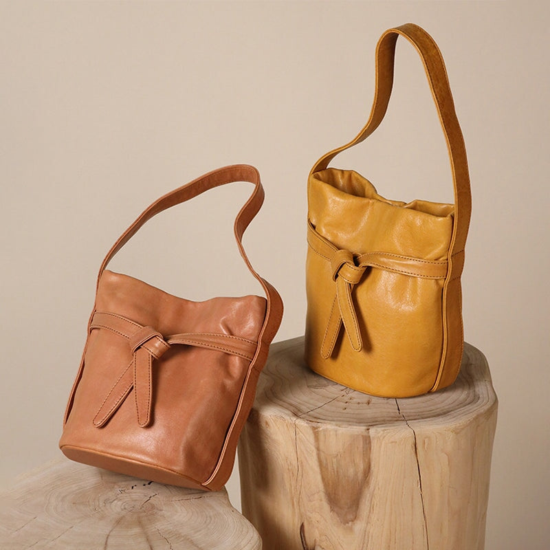 Full-grain leather bucket bag with knot-belt detail in light yellow and orange, styled on wood stumps