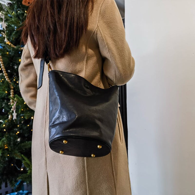 Women wearing a black vegetable tanned leather bucket bag as a shoulder crossbody with gold hardware.
