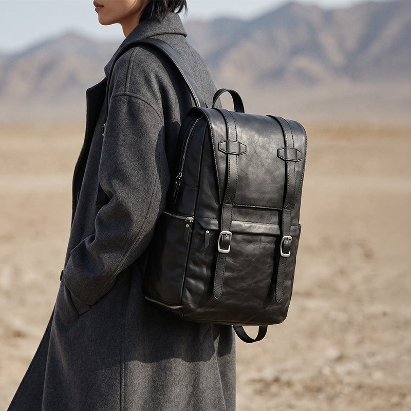Black vegetable-tanned leather camera backpack with gold-tone hardware and adjustable straps — front view
