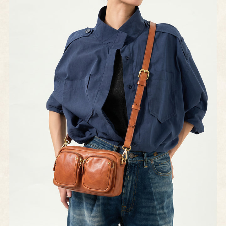 Vegetable tanned leather camera bag with two front zip pockets, shown in honey brown crossbody style.