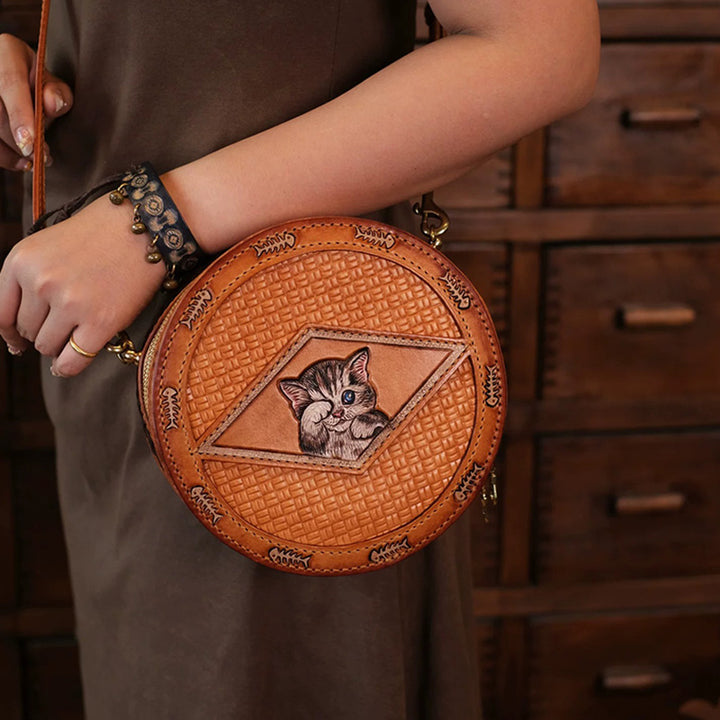 Woman holding a tan hand-tooled leather cat round crossbody bag by its strap
